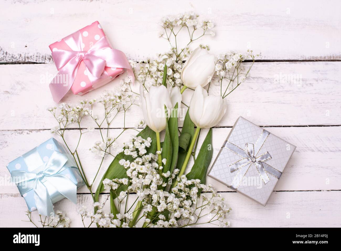 Frühlings-Tulpenblumen, Geschenkbox und Papierkarte auf grauem Steintisch von oben in flacher Laienform. Begrüßung für Frauen oder Mütter Stockfoto