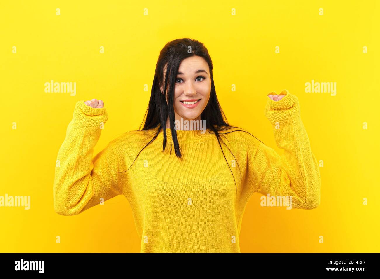 Brünette Mädchen ihren Erfolg und Sieg ballte die Fäuste mit Freude Freude. Glücklichen Frau in einem gelben Pullover in die Kamera lächeln Stockfoto