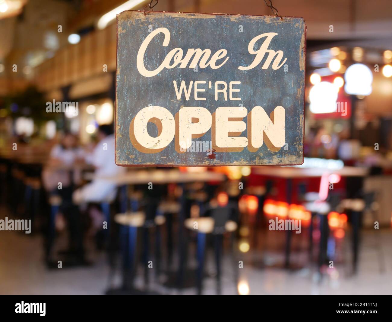 Ein Business Vintage Schild, das auf dem Cafe/Restaurant Fenster steht: „Come in We're Open“. Bild von abstrakten Unschärfe Restaurant mit Menschen. Stockfoto