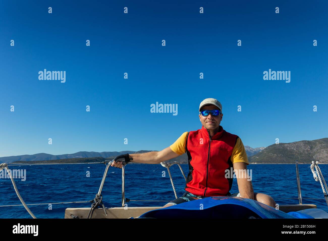 Ein Mann auf einer Yacht sitzt auf einem Deck im Hintergrund der Inseln. Stockfoto