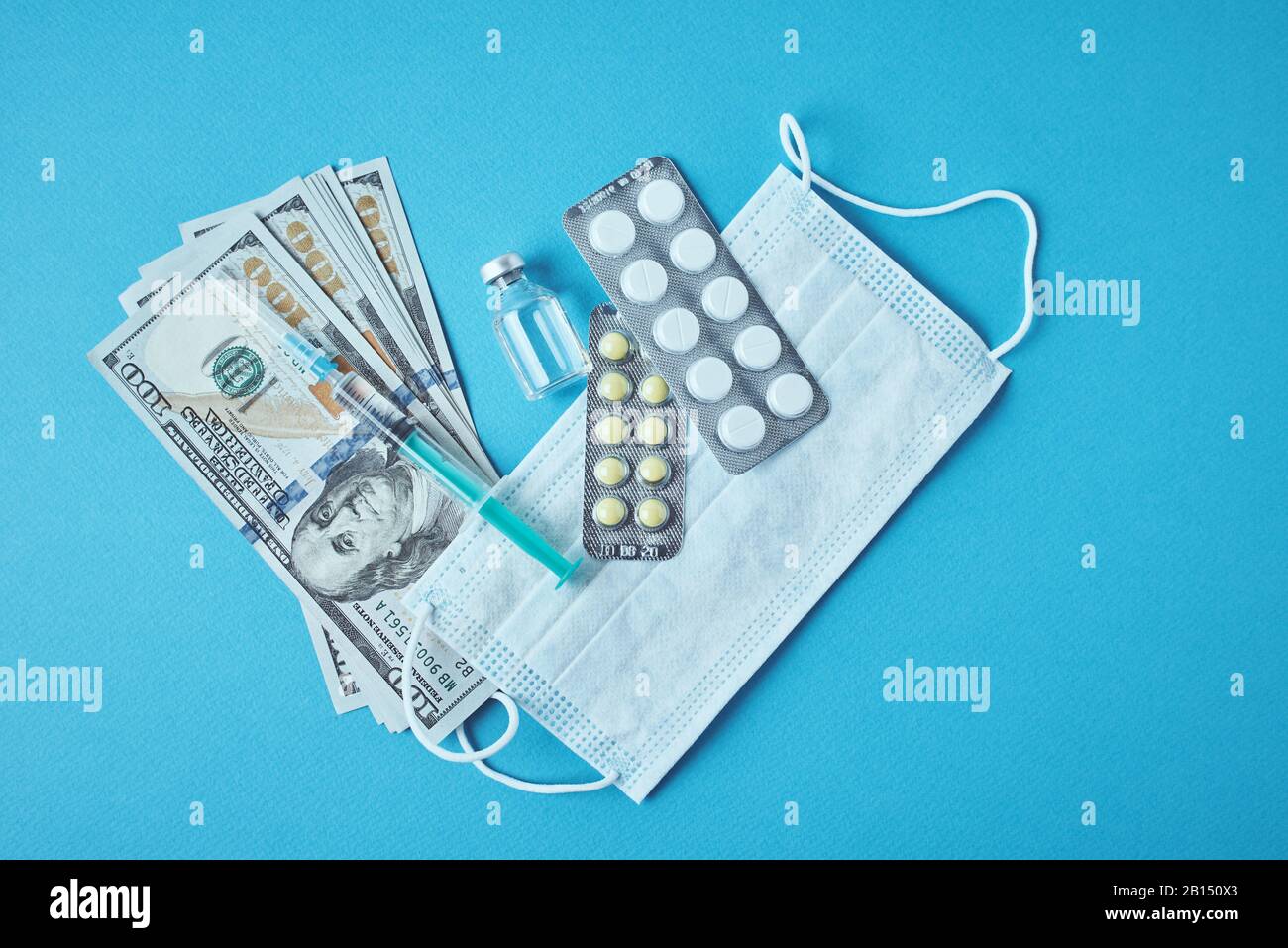Pillen, Schutzmaske und Dollarscheine auf blauem Hintergrund. Teures Medizinkonzept. Pharmaindustrie und Krankenversicherung Stockfoto