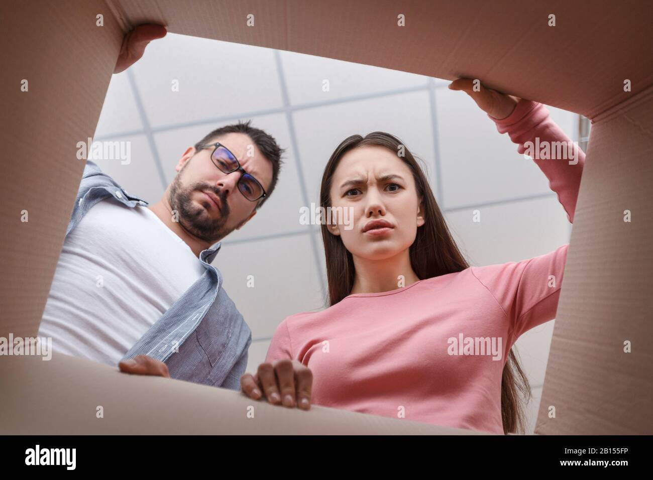 Enttäuschte Paare packen Karton aus und sind verwirrt Stockfoto