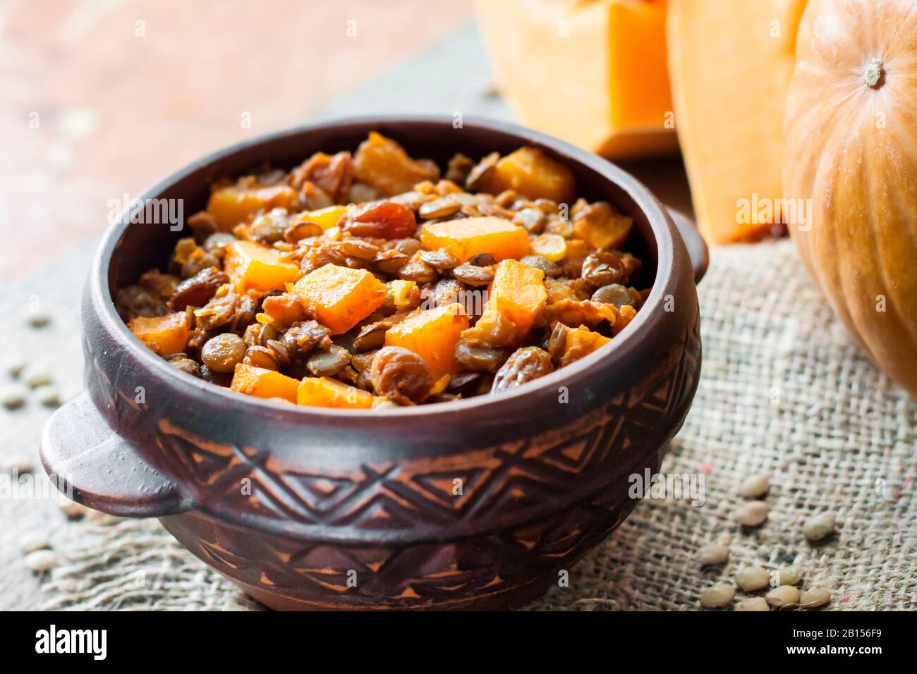 Hausgemachte würzige Curry mit grünen Linsen, Kürbis und Rosinen in rustikaler Keramikschale Stockfoto