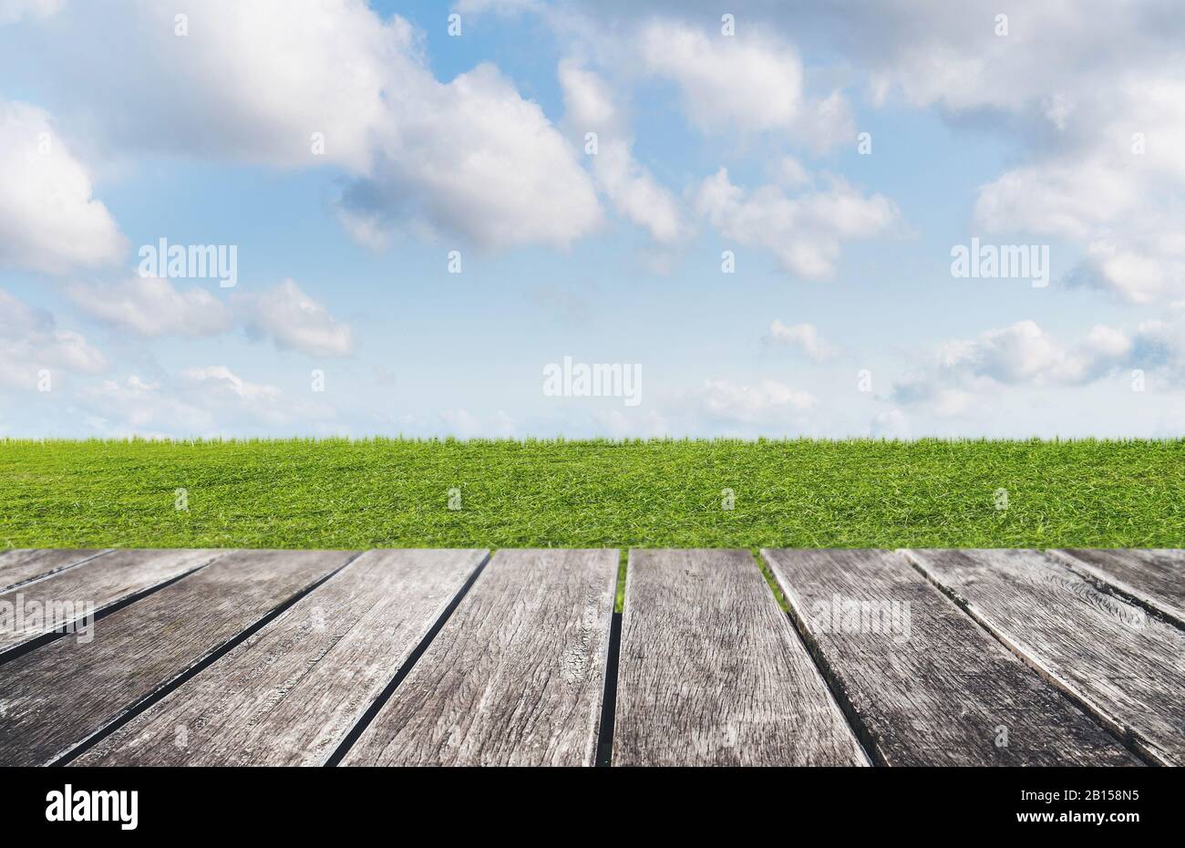 Grünes Gras, blauer Himmel und weiße Wolken mit Holzfußboden Stockfoto