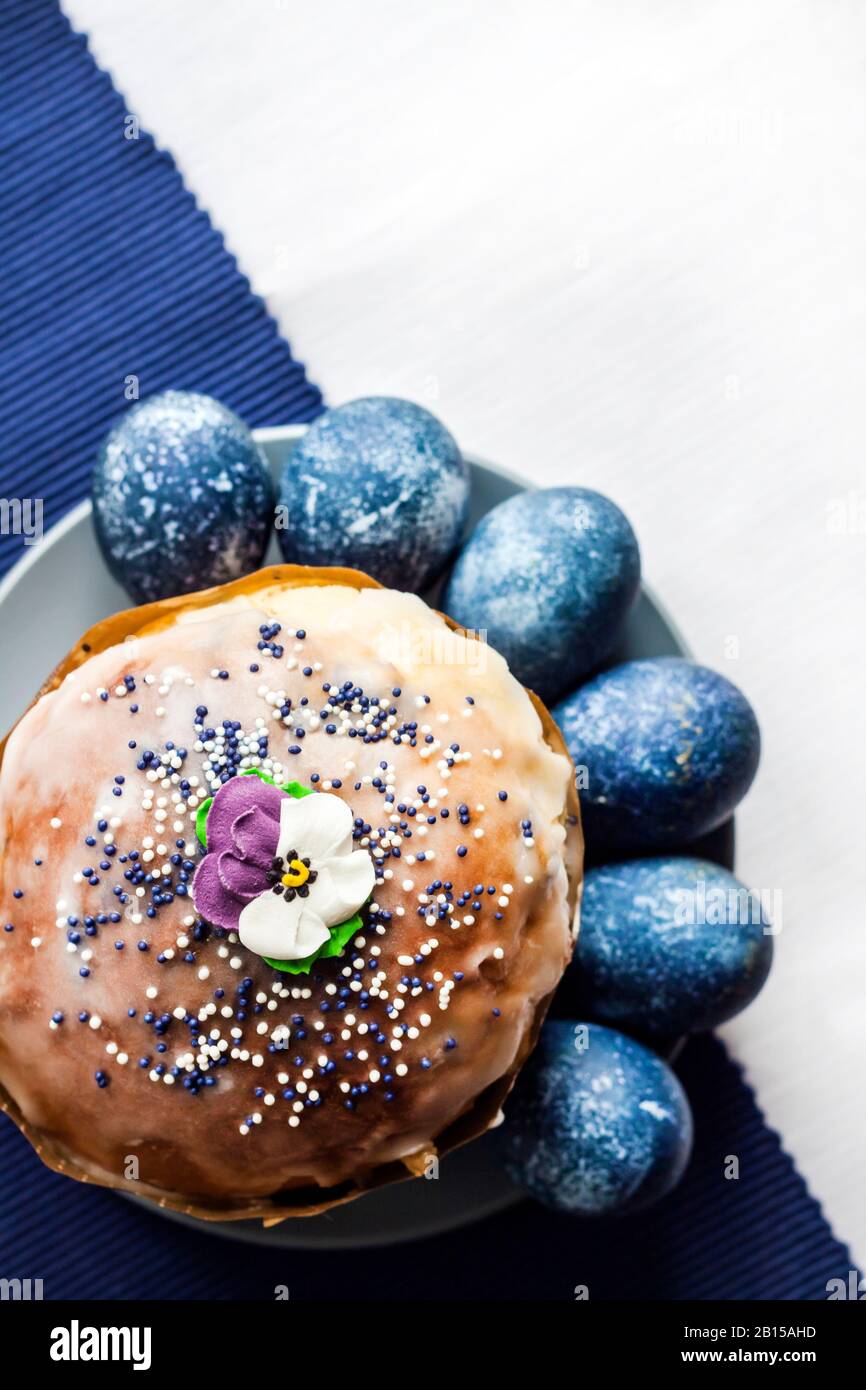 Osterkuchen mit Zuckerblume und blau gefärbten Eiern auf einem Teller auf weißem und blauem Stoffhintergrund mit Kopierraum. Eier waren blau-Wi-farbig Stockfoto