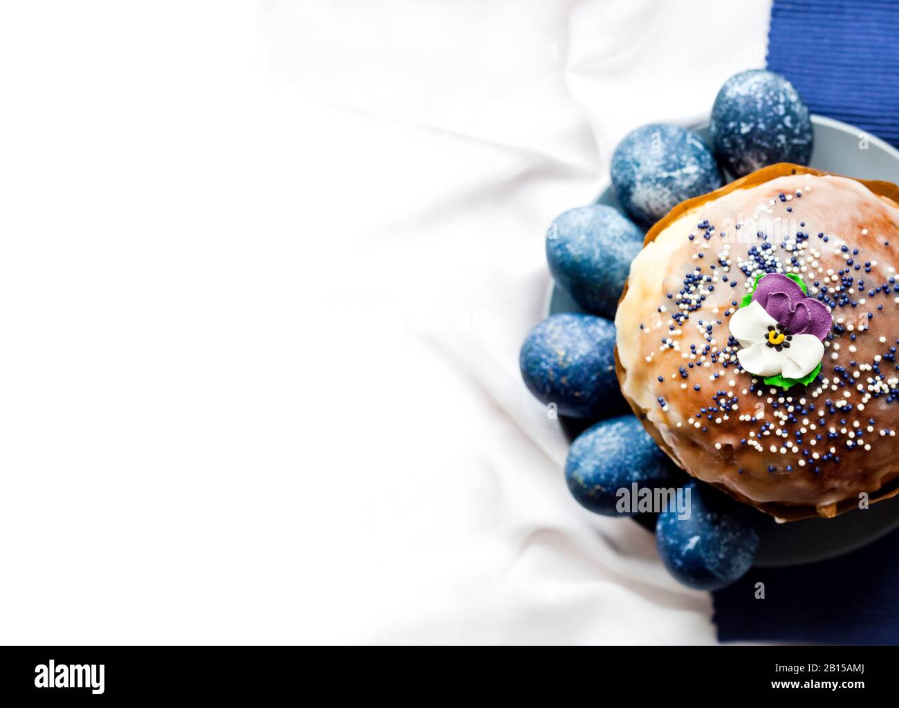 Osterkuchen mit Zuckerblume und blau gefärbten Eiern auf einem Teller auf weißem und blauem Stoffhintergrund mit Kopierraum. Eier waren blau-Wi-farbig Stockfoto