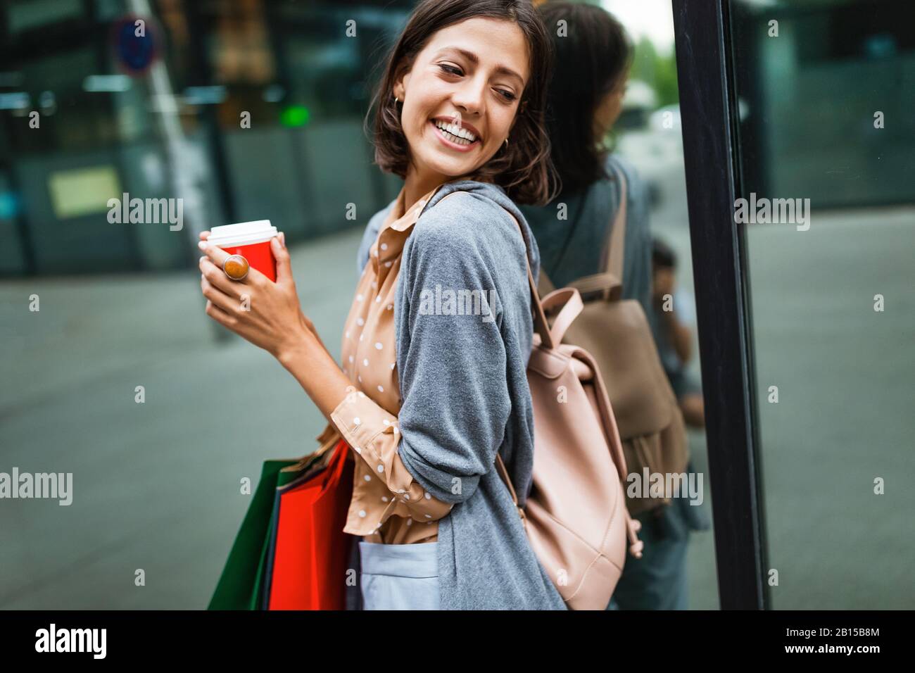 Fröhliche junge Frau, die nach dem Einkaufen in der Stadt Kaffee trinkt und mit Taschen spazieren geht. Stockfoto