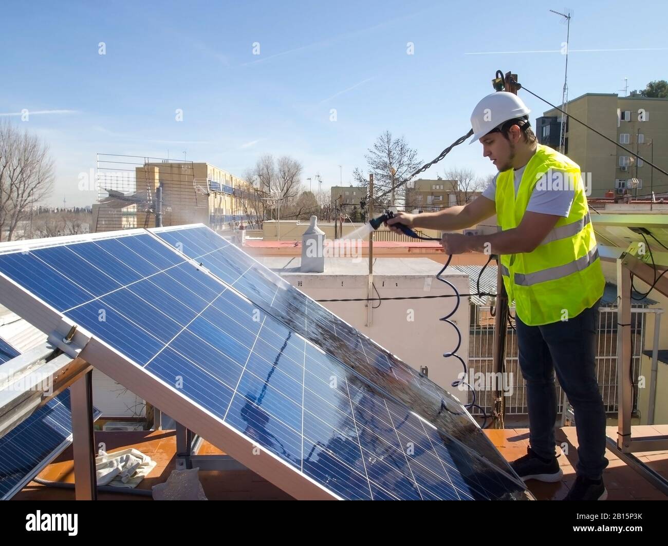 Kaukasisch attraktiver junger Techniker, der Solarpaneele mit einem Schlauch reinigt. Alternative Stromquelle, nachhaltige Ressourcenkonzeption. Stockfoto