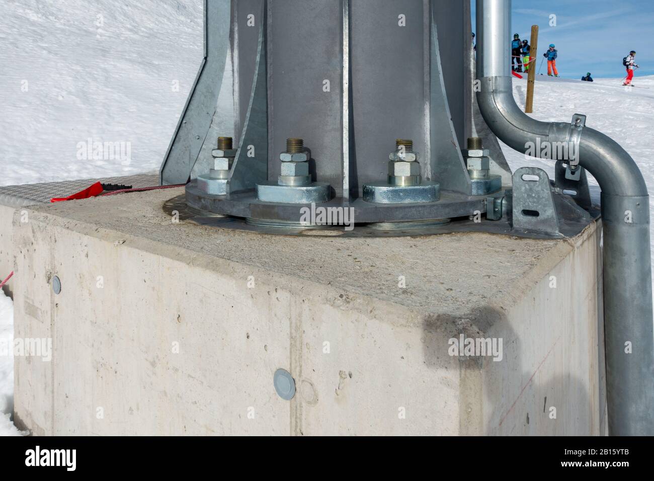 In den schneebedeckten Bergen ist eine Stahlsäule mit riesigen Schrauben an einem Betonfundament befestigt Stockfoto