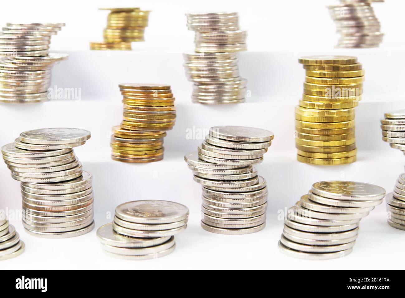 Volatilität der Währung während einer Krise. Säulen verschiedener instabiler Metallmünzen auf weißen Stufen Stockfoto