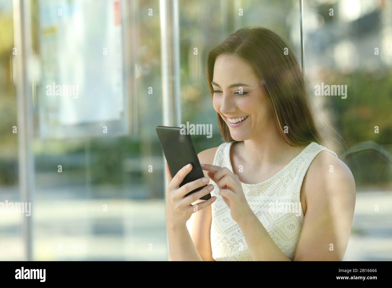 Fröhliche junge Frau überprüft Smartphone und wartet auf den Bus Stockfoto