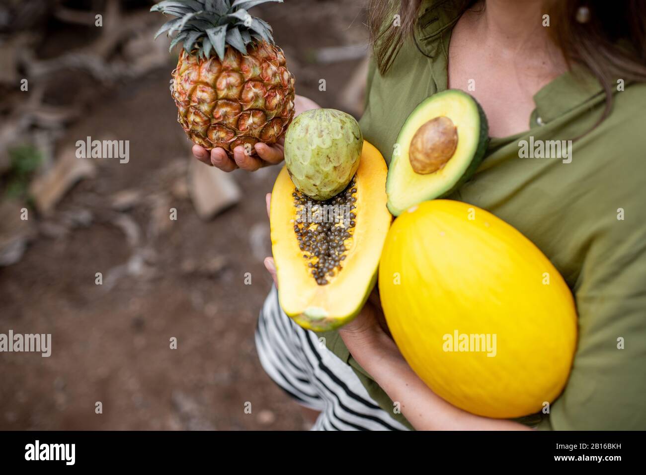 Frau mit exotischer Küche im Freien, in der Nähe von Ananas, Papaya, Melone, Avocado und Cherymoya-Früchten. Konzept von Vegetarismus, gesundem Essen und Wohlbefinden Stockfoto