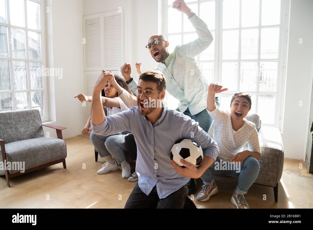 Aufgeregte multiethnische Freunde feierten den Fußballsieg im Innenbereich Stockfoto