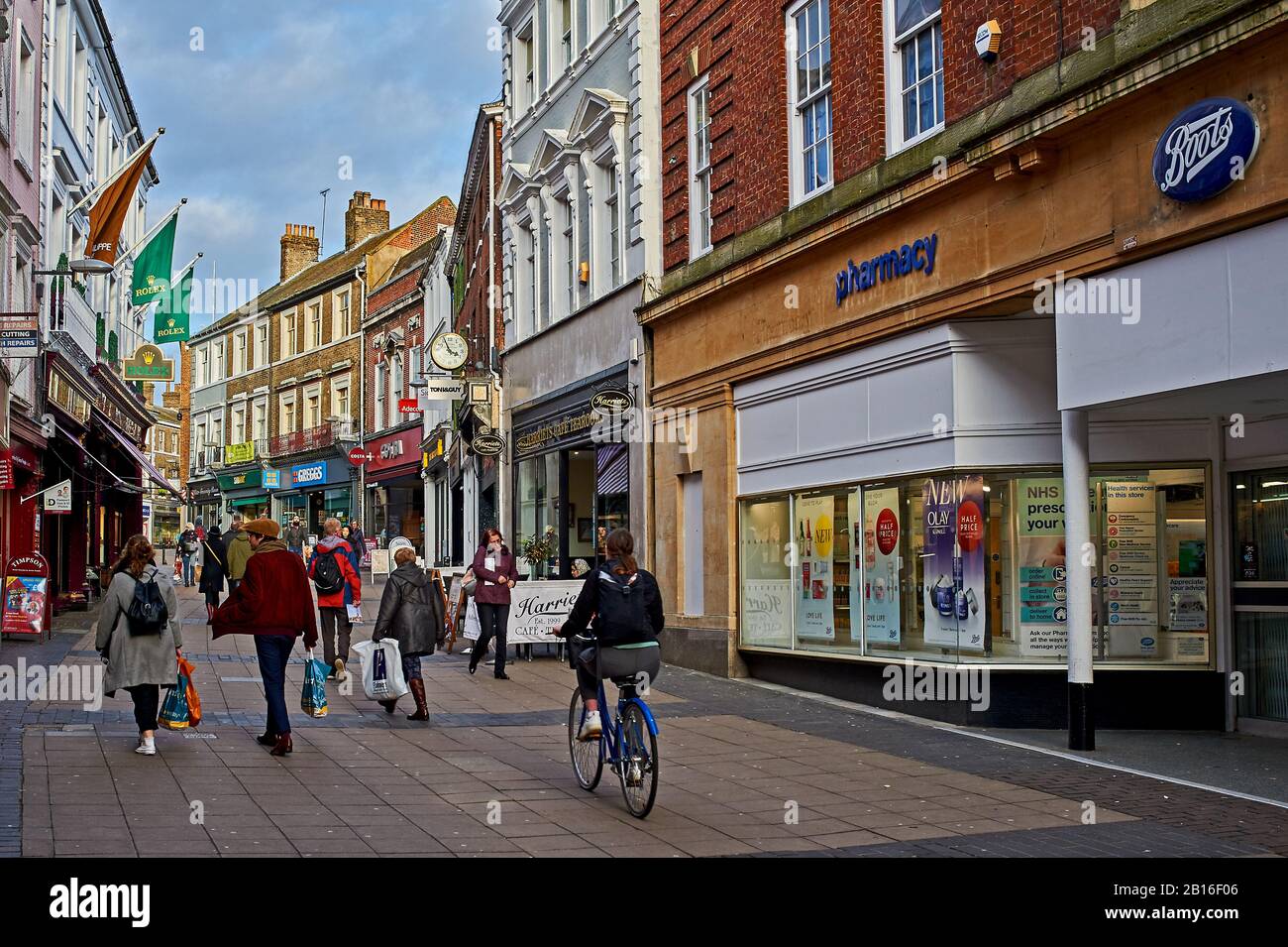 Straßenszene im Stadtzentrum von Norwich mit Menschen, die an Geschäften und Büros vorbeilaufen und mit dem Fahrrad fahren Stockfoto