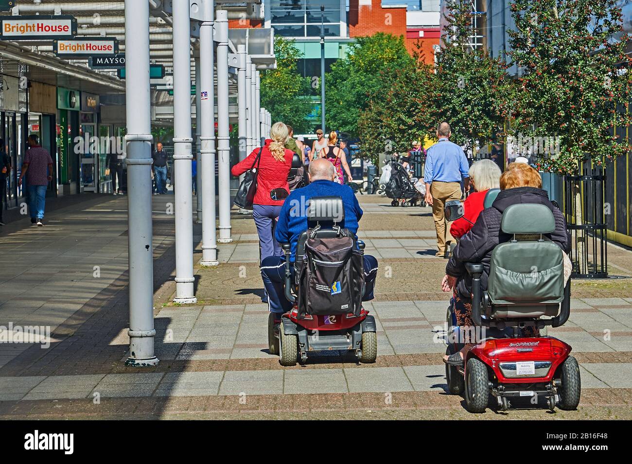 Menschen mit Rollern für Mobilität, die durch die Fußgängerzone im Stadtzentrum von Stevenage fahren Stockfoto