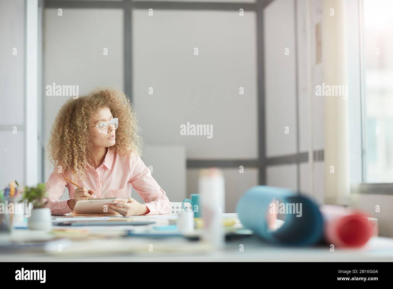 Porträt einer funky jungen Geschäftsfrau, die eine Brille trägt, die auf Fenster blickt, während sie am Arbeitsplatz träumt, Platz für Kopien Stockfoto