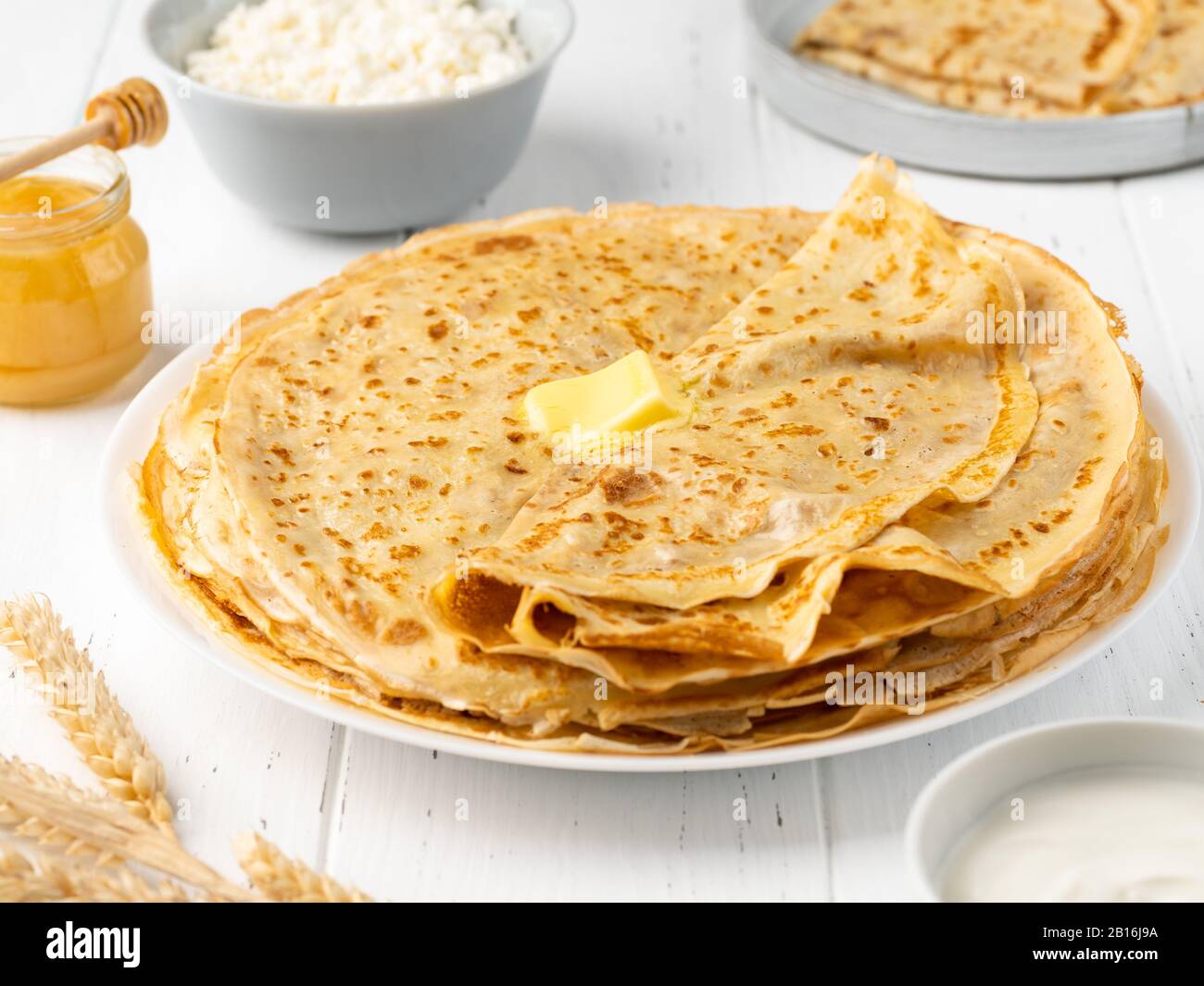 Crepes mit Butter, Honig, Sauerrahm, Hüttenkäse und Weizenkorn auf weißem Holzhintergrund. Hausgemachtes gesundes Frühstück. Stockfoto