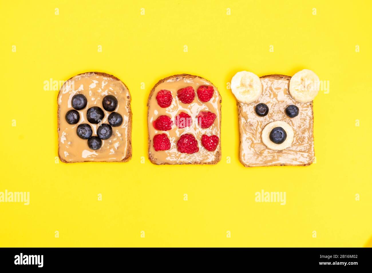 Draufsicht über lustige Kinder Erdnussbutter-Toast mit Blaubeere, Banane, Himbeere auf gelbem Hintergrund Stockfoto