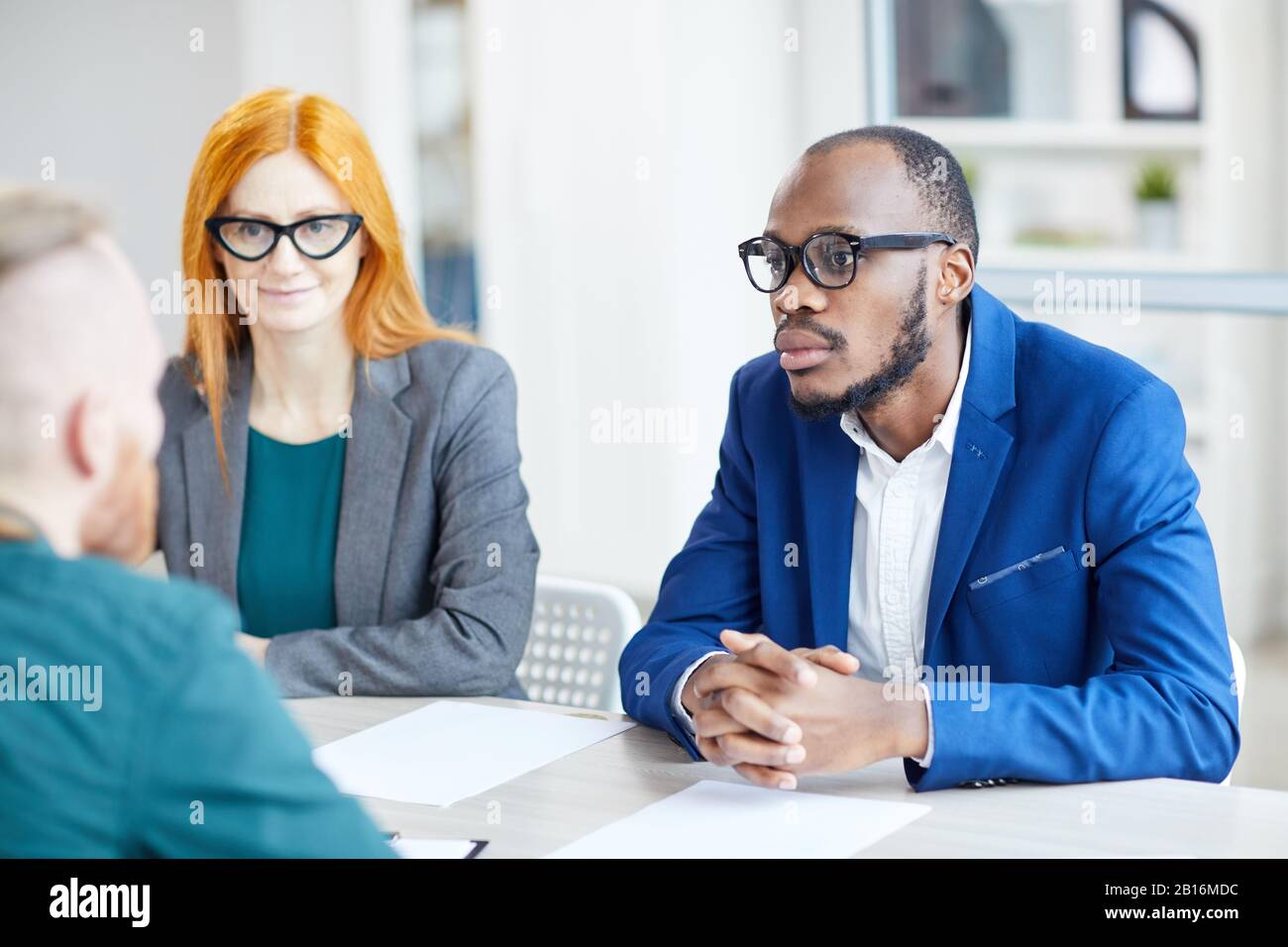 Porträt eines zeitgenössischen afroamerikanischen Geschäftsmannes, der während eines Bewerbungsgesprächs im Büro dem Kandidaten zuhört Stockfoto