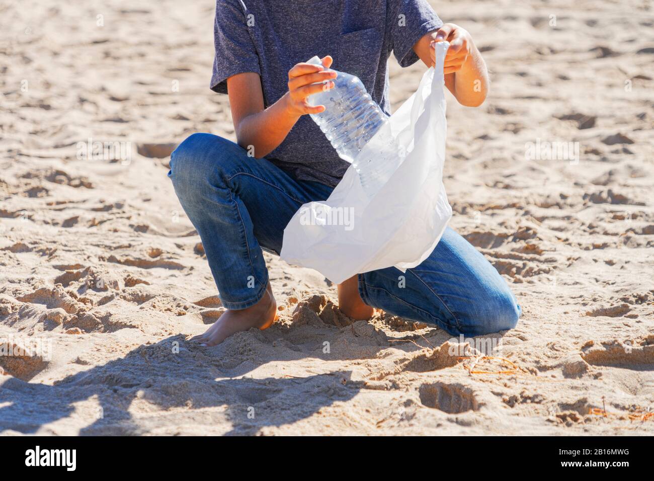 Strand aus Plastikmüll reinigen. Nehmen Sie die Plastikflasche aus dem Sand und legen Sie sie zum Recycling in einen Plastikbeutel Stockfoto