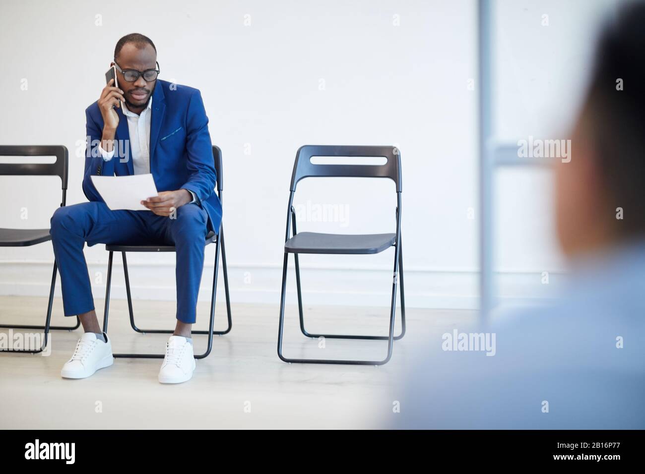 Komplettes Portrait eines modernen afroamerikanischen Mannes, der auf ein Bewerbungsgespräch hinter der Glaswand wartet und per Telefon spricht, Copy-Space Stockfoto