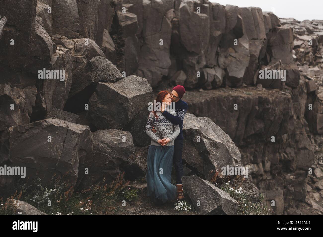 Liebespaar in Island. Vulkanischer Hintergrund aus Stein. Dramatische nordische Landschaft, kaltes Wetter. In traditionellen Wollpullovern, Jeans und grauem Rock. Stockfoto