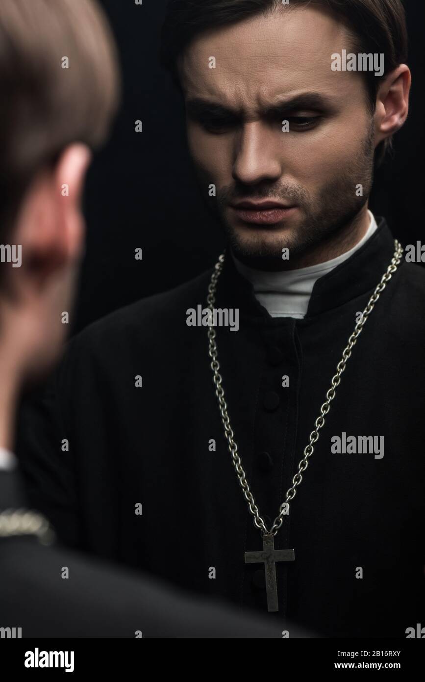 Junger seriöser katholischer Priester denkt, während er in der Nähe der eigenen Reflexion steht, isoliert auf Schwarz Stockfoto
