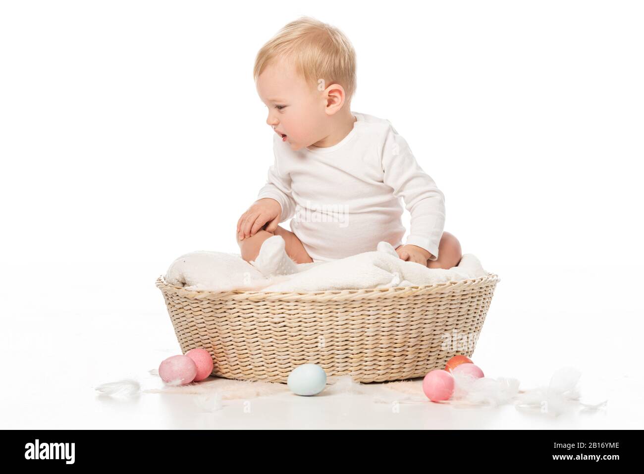 Kind, das hinunterblickt und in einem Korb sitzt, mit Ostereiern auf weißem Hintergrund Stockfoto