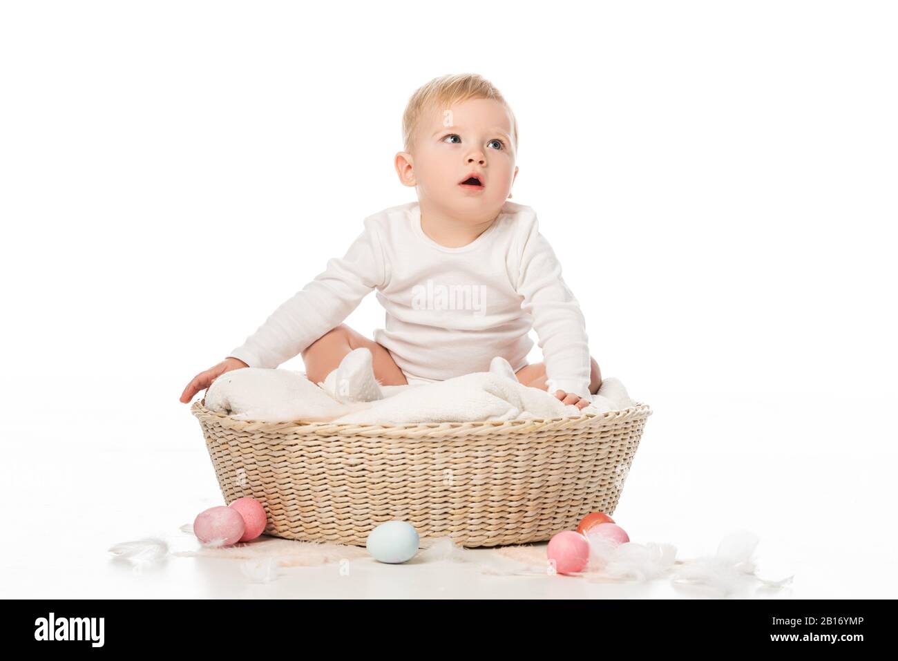 Kind mit offenem Mund auf Decke im Korb mit Ostereiern auf weißem Hintergrund Stockfoto