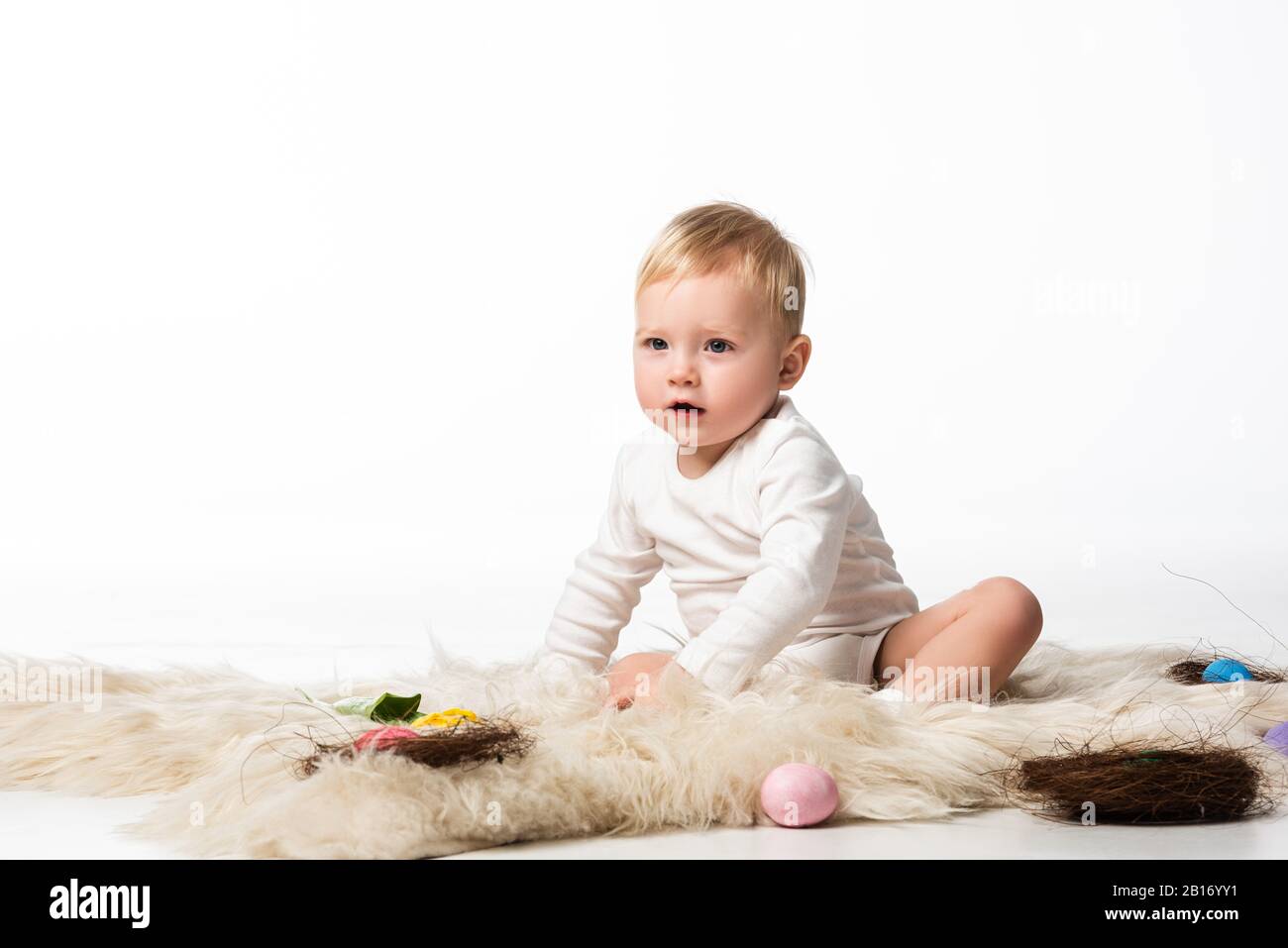 Kind mit offenem Mund, auf Pelz mit Nestern und ostereiern auf weißem Grund Stockfoto