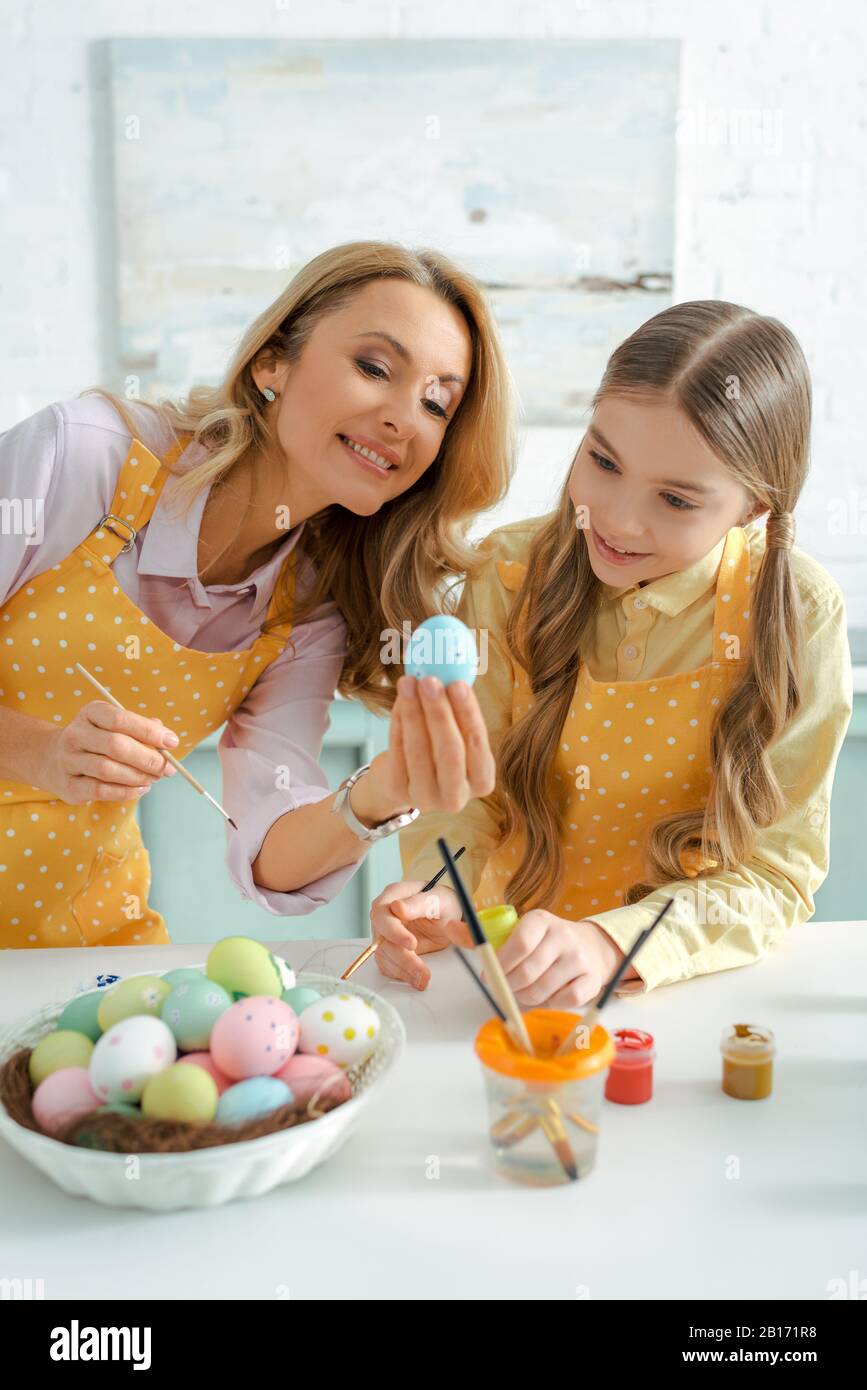 Fröhliche Frau und liebenswürdig liebes Kind, das an ostern ein gemaltes Hühnerei betrachtet Stockfoto