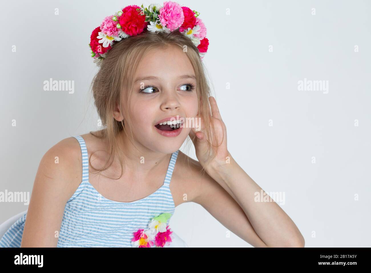Glückliches Kind Mädchen Hand zu Ohr Abhören versuchen, ein Chitchat zu hören. Nahaufnahme des kaukasischen Kindermodells mit geblümtem Kopfband, isoliert auf der weißen gra Stockfoto