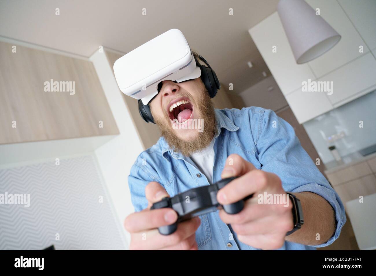 Aufgeregter junger Mann mit vr-Brille, die den Controller beim Spielen von Videospielen hält Stockfoto