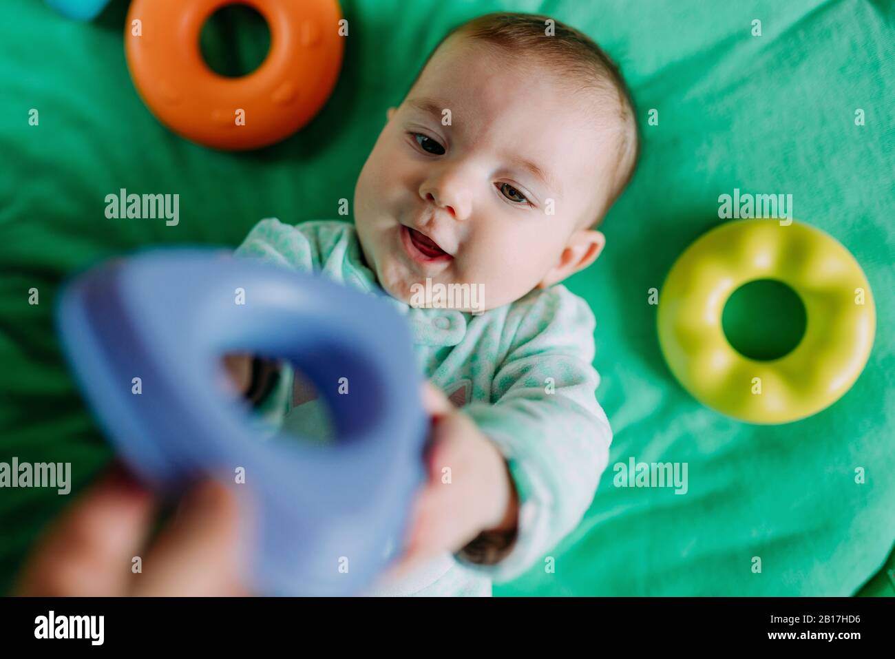 Porträt von Baby Mädchen auf grünen Matte liegend mit Kunststoff-Spielzeug spielen Stockfoto