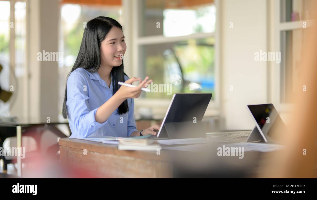 Zugeschnittene, lächelnde Geschäftsfrau, während sie sich mit ihrer Arbeit mit der Mitarbeiterin berät, während sie in einem einfachen Arbeitsraum sitzt Stockfoto
