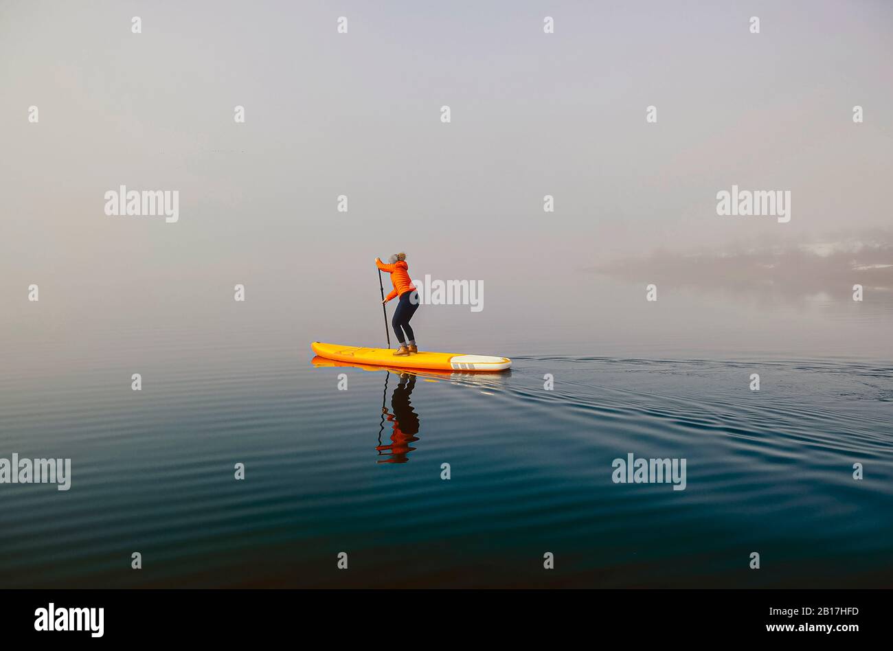Frau steht auf Paddelsurfen auf einem See im Nebel Stockfoto