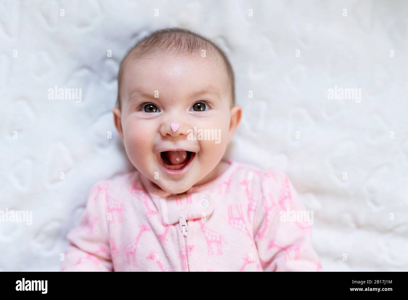 Porträt von glücklichen Mädchen mit rosa herzförmigen Süßigkeiten auf der Nase Stockfoto