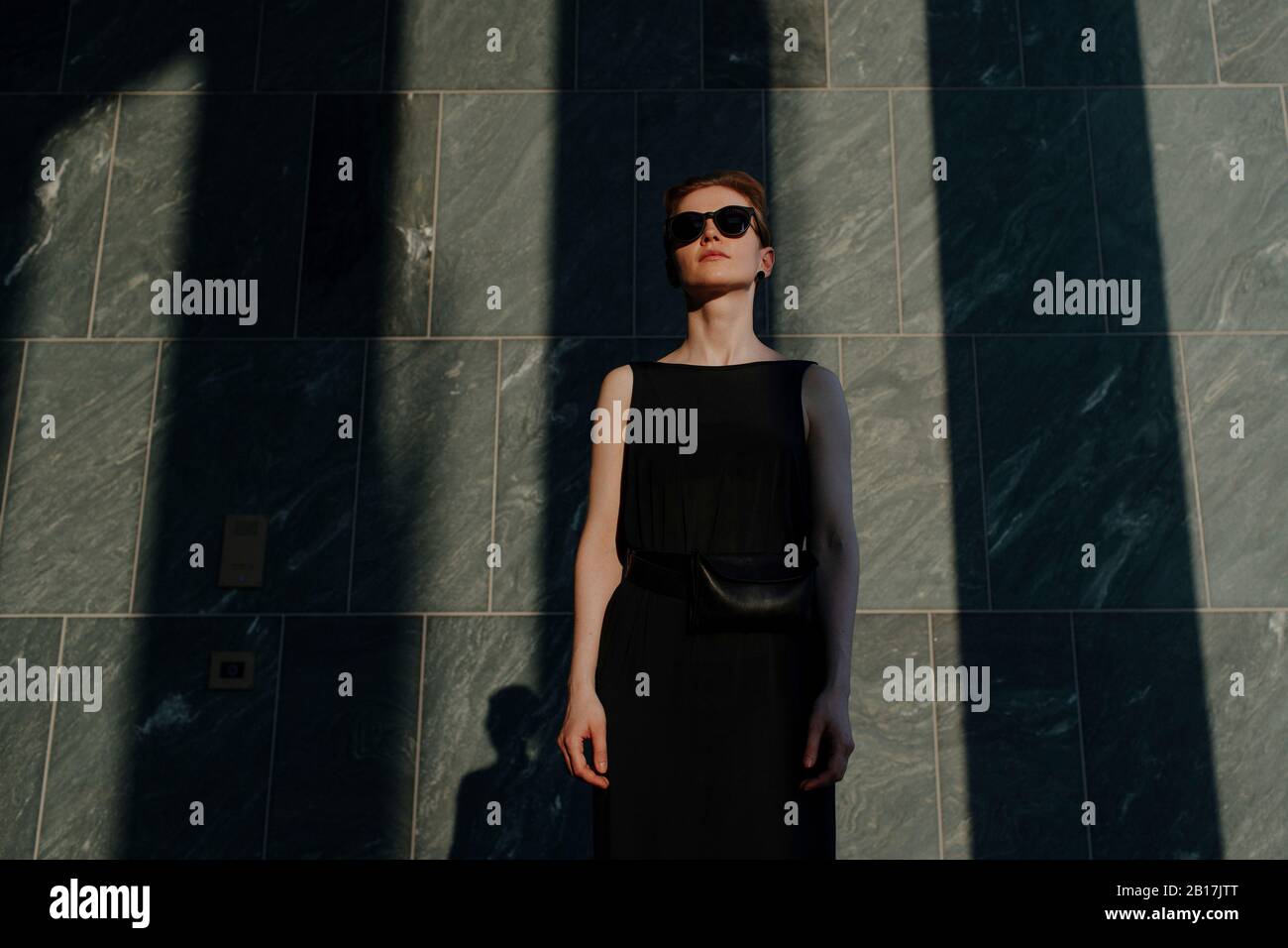 Rothaarige Frau mit Sonnenbrille, vor Steinwand mit Schatten Stockfoto