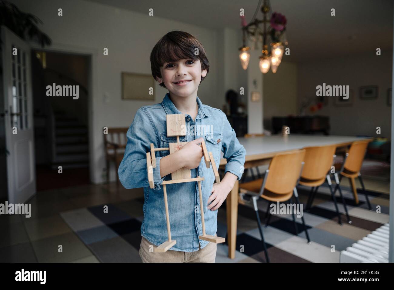 Kleiner Junge, der im Speisesaal steht und selbstgemachten Spielzeugroboter hält Stockfoto