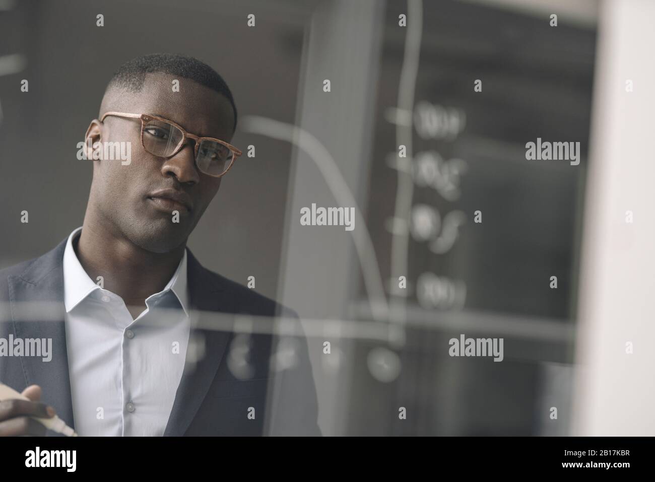 Porträt des jungen Geschäftsmannes, das Diagramm auf der Glasscheibe im Büro betrachtet Stockfoto
