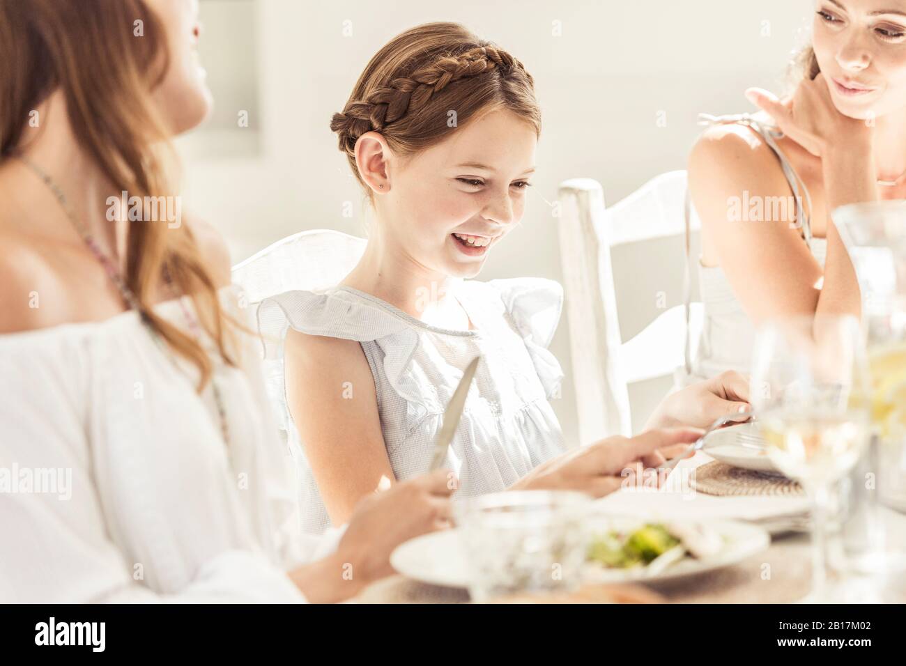 Fröhliches Mädchen und zwei Frauen beim gemeinsamen Mittagessen Stockfoto