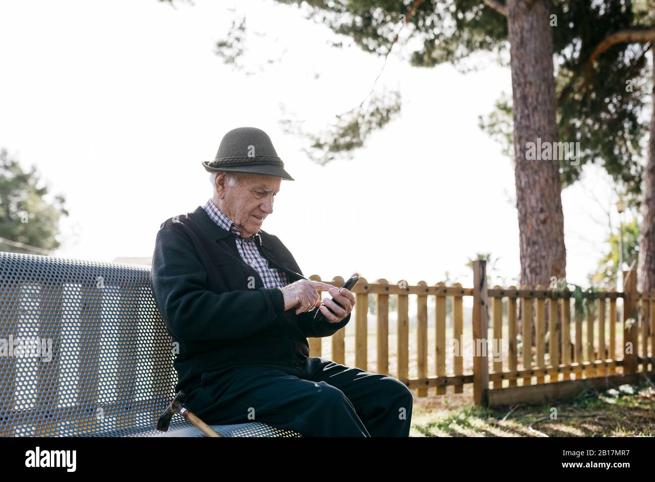 Alter Mann mit, auf Bank sitzend, Smartphone verwendend Stockfoto