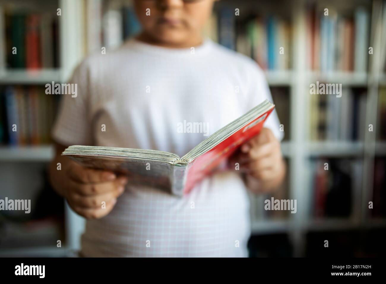 Junge, der vor Bücherregalen steht und ein Buch hält, Nahaufnahme Stockfoto