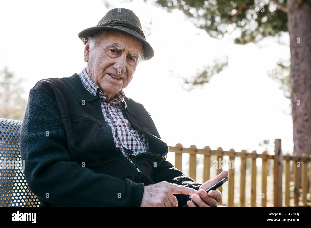Alter Mann mit, auf Bank sitzend, Smartphone verwendend Stockfoto