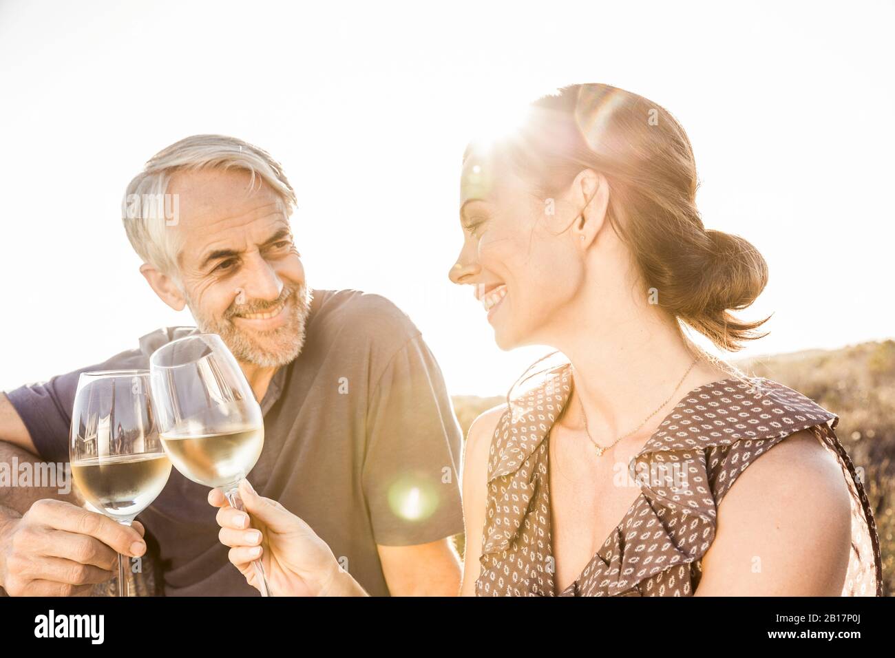 Glückliches Paar, das ein Glas Weißwein bei Sonnenuntergang hat Stockfoto