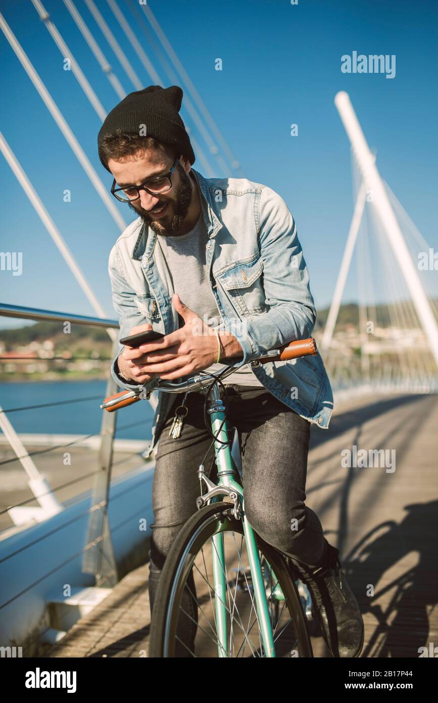 Junger Mann pendelt in der Stadt mit seinem fixie Fahrrad, mit dem Smartphone Stockfoto