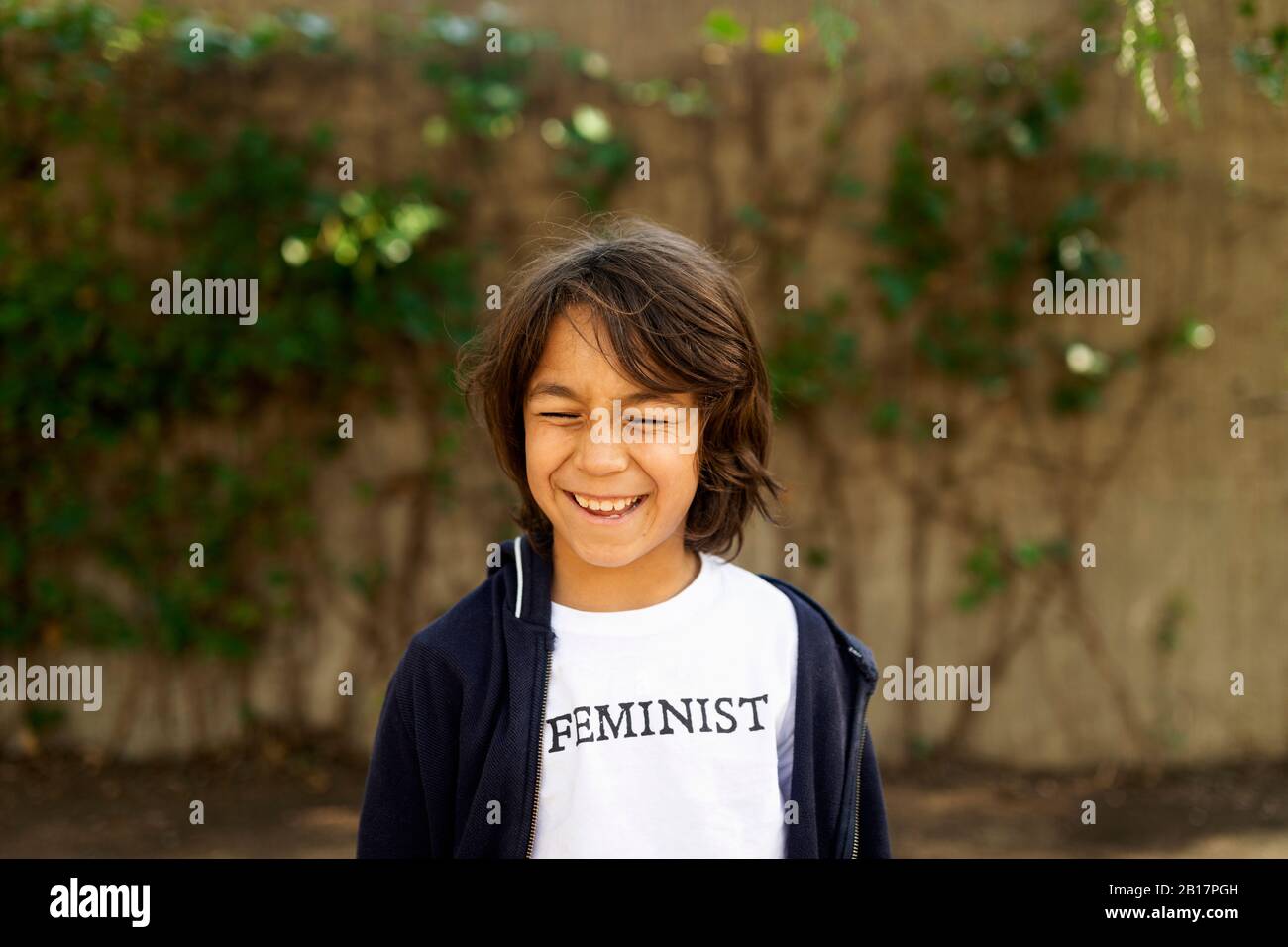 Lachender Junge, der auf der Straße mit Aufdruck auf dem T-Shirt steht und feministisch sagt Stockfoto