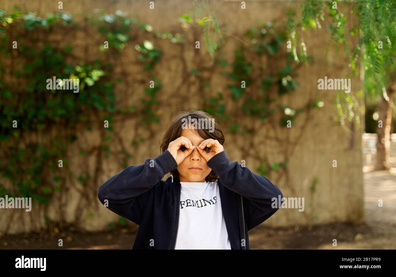 Kleiner Junge, der durch die Finger schaut, mit Aufdruck auf T-Shirt, sagt Feminist Stockfoto