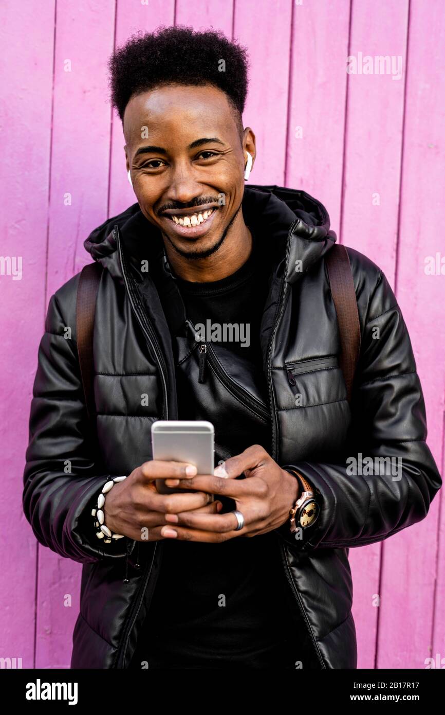 Porträt eines lächelnden Mannes mit Smartphone und drahtlosen Kopfhörern im Freien Stockfoto
