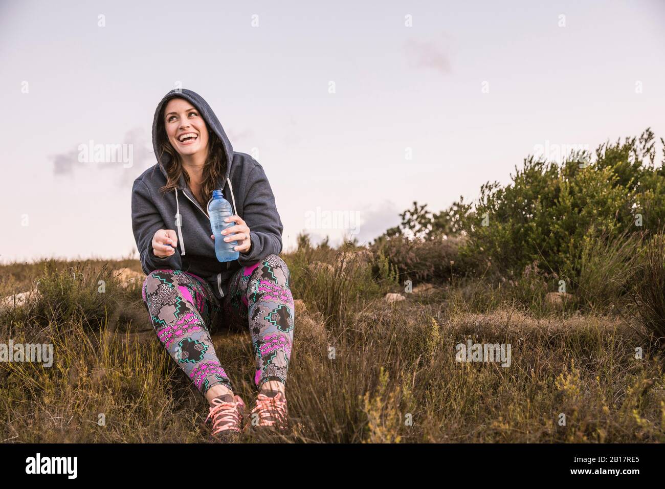 Glückliche Frau mit einer Flasche Wasser, die eine Pause vom Sport auf dem Land macht Stockfoto